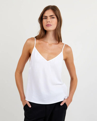 Woman wearing a white spaghetti strap top against a plain background