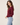 A woman wearing a burgundy knit sweater and light blue jeans, photographed from the back against a plain light beige studio background.