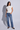 A woman modeling a white short-sleeve button-front top and blue straight-leg jeans against a light gray studio background.
