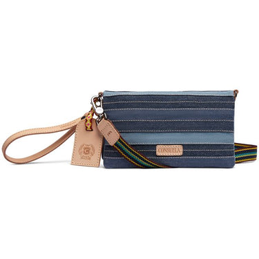A Consuela wristlet clutch in a blue and navy striped fabric, featuring a tan leather wristlet strap and a matching leather hangtag, with a colorful woven strap detail.