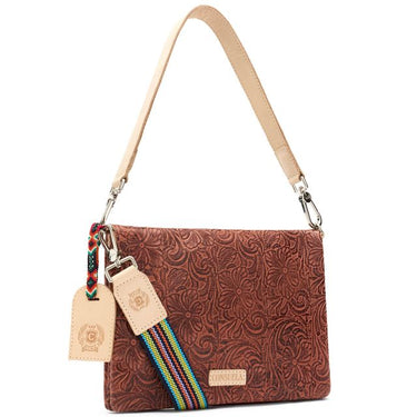 A brown embossed leather shoulder bag with a floral pattern, featuring a light beige leather strap, a colorful woven strap detail, and a matching leather hangtag on a white background.