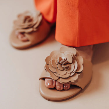 Beige sandals with floral designs worn by a person in orange pants.