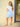 Woman wearing a white top and blue patterned skirt standing against a beige wall.