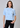 a woman wearing a blue knit short sleeve sweater with sparkling floral embellishments and black pants on a neutral background