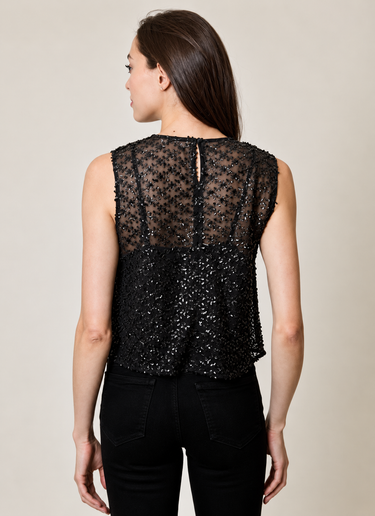 A woman wearing a black mesh, sheer embellished tank with a black tank underneath and black jeans