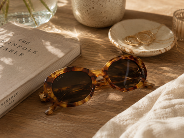 Tortoiseshell sunglasses on a wooden surface with a book and decorative items.