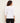 A woman shown from the back wearing a white three-quarter sleeve top and black pants, standing against a plain off-white studio background.