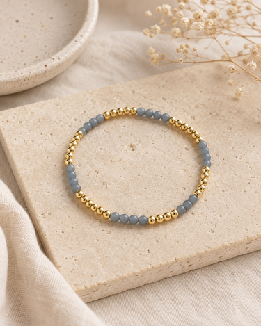 a light blue and gold beaded bracelet on a neutral background