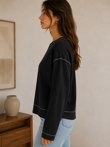 Woman wearing a black sweater with white trim in a room with a wooden cabinet and vase.