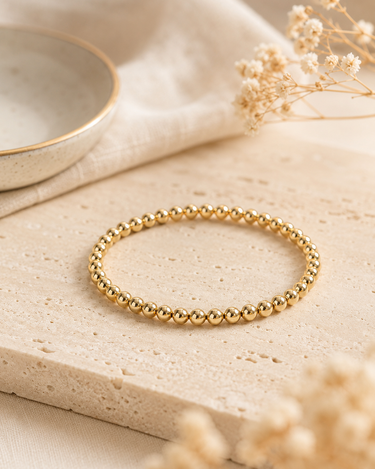 a 4mm gold beaded bracelet on a neutral background