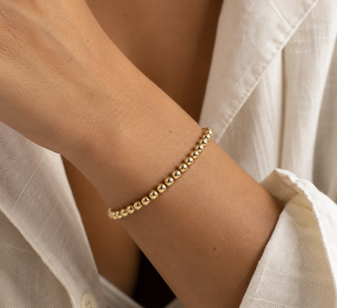 a woman wearing a 4mm gold beaded bracelet on a neutral background