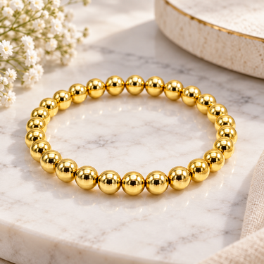 A gold beaded stretch bracelet made of polished metallic spherical beads, displayed on marbled table.