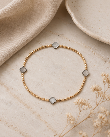 A gold beaded bracelet with mother of pearl clover charms on a table