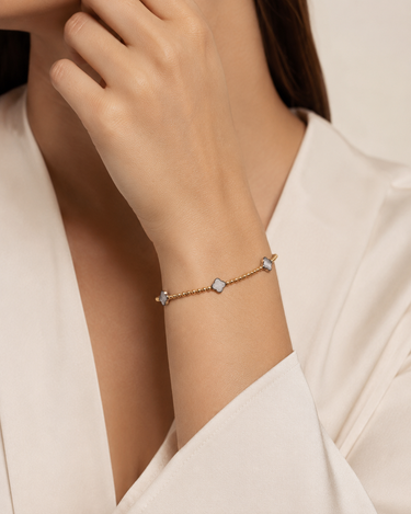 a woman wearing gold beaded bracelet with mother of pearl clover charms