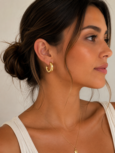 Woman wearing gold hoop earrings and a necklace against a neutral background