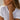A close-up lifestyle shot of a woman wearing a delicate gold beaded bracelet on her wrist, paired with a white t-shirt and gold hoop earrings.
