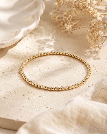 a 3mm gold beaded bracelet on a neutral background