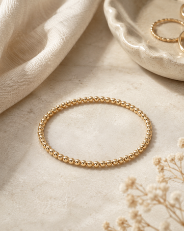 a 3mm gold beaded bracelet on a neutral background