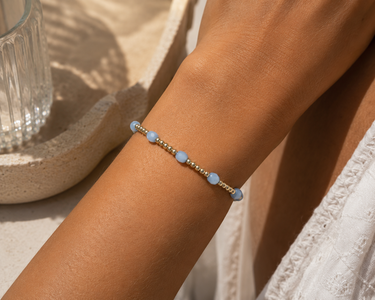 a woman wearing a gold beaded bracelet with blue beaded accents
