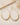 A pair of gold teardrop hoop earrings with a beaded lower section and a single silver oval bead at the center, displayed on a neutral beige surface with dried floral accents.