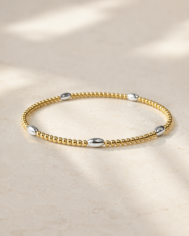 a oval silver and circle gold beaded bracelet on a neutral background