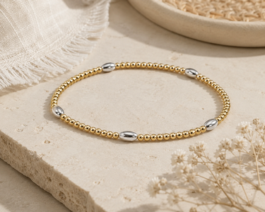 a oval silver and circle gold beaded bracelet on a neutral background