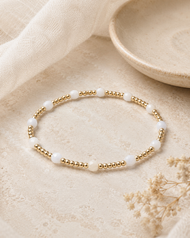 a gold and white beaded bracelet on a neutral background