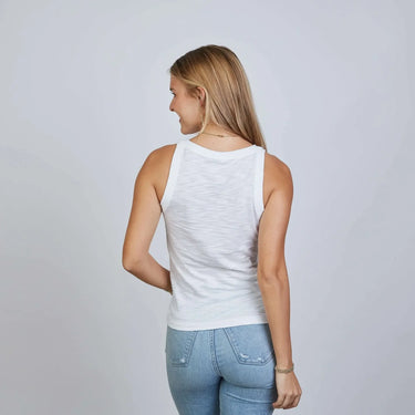 Woman wearing a white tank top and light blue jeans on a plain background
