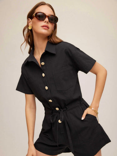 Woman wearing a black romper with gold buttons against a beige background