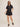 Woman wearing a black romper with buttons on a beige background