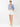 A woman modeling a blue and white vertically striped button-down shirt with rolled sleeves and white shorts, standing against a plain white studio background.