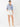 A woman modeling a blue and white vertically striped button-down shirt with rolled sleeves, paired with white shorts and beige heeled sandals, against a plain white studio background.