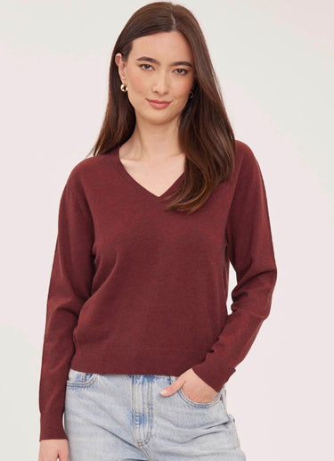 a woman wearing a deep wine red v-neck pullover sweater and blue jeans on a white background
