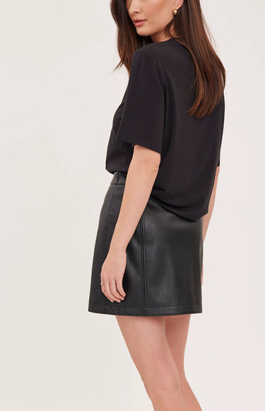 A woman facing backwards wearing a black tee, faux leather skirt in black on a white background.