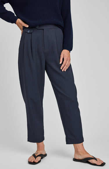 Person wearing navy pleated pants and a navy sweater on a light gray background