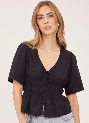 A woman wearing a v neck poplin top with ruching at the center on a white background
