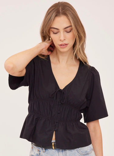 A woman wearing a v neck poplin top with ruching at the center on a white background