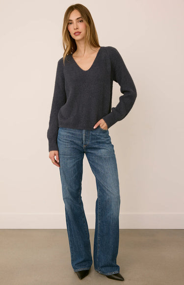 A woman wearing a gray ribbed v-neck sweater and jeans on a white background
