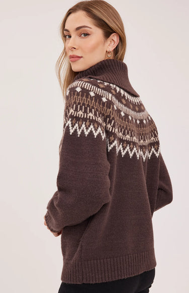 A woman facing backward in a brown turtle neck with a fair isle print and black jeans on a white background.