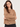 A woman wearing a textured knit button-front cardigan in a warm camel brown color, paired with black pants, against a plain light gray studio background.
