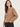 A woman wearing a textured knit cardigan sweater in a warm camel brown color, paired with black jeans, against a plain light gray studio background.