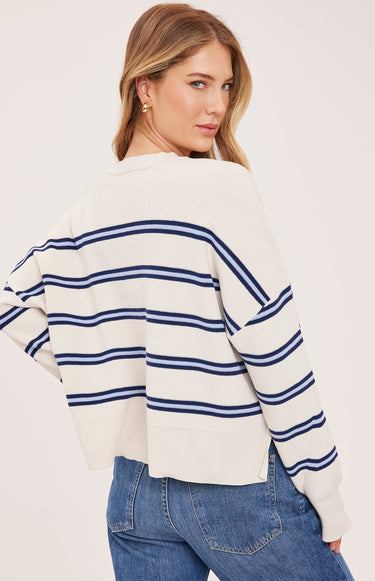 A woman wearing a cream and navy stripe oversized sweater and blue jeans on a white background