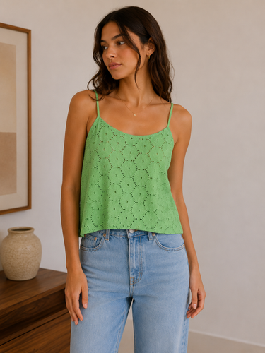 Woman wearing a green lace top and blue jeans in a room with a wooden shelf and framed picture.