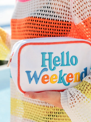 White pouch with 'Hello Weekend' text held by a person wearing a colorful mesh top.