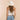 Person wearing a white tank top, blue jeans, and a white sun hat on a beige background