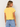 A woman shown from the back wearing a bright yellow short-sleeve crop top and light blue jeans against a plain off-white background.