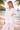 Woman in a white outfit standing on a beach with palm trees and water in the background