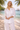 Woman in white outfit standing on a beach with palm trees and a clear sky.