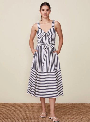 Woman wearing a striped dress standing on a woven mat with a beige background