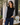 a woman wearing a black crew neck with black and white polo stripe sleeves and blue jeans on neutral background.